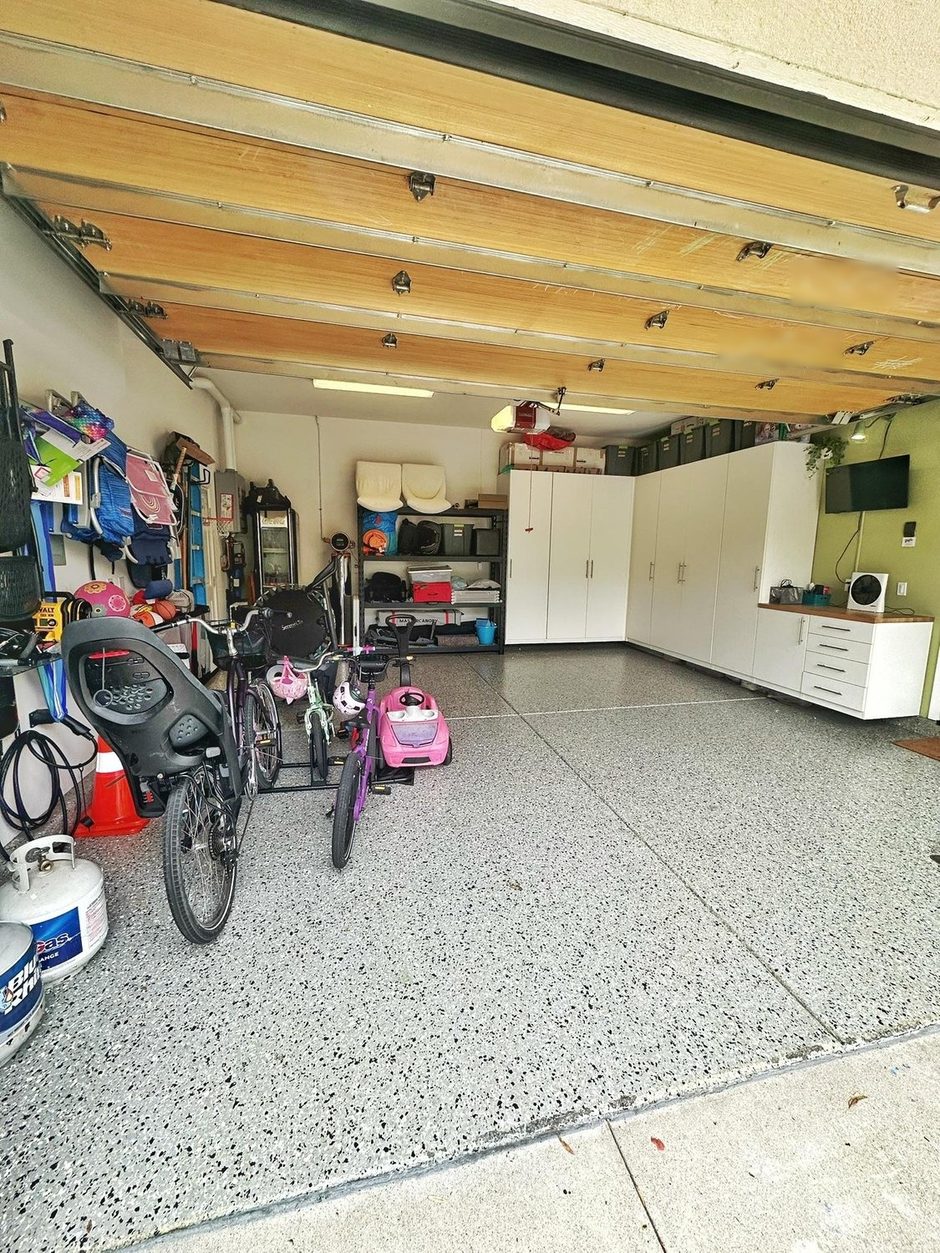 The same garage from the driveway after: clear speckled floor, bikes on a rack, white cabinets along the back wall
